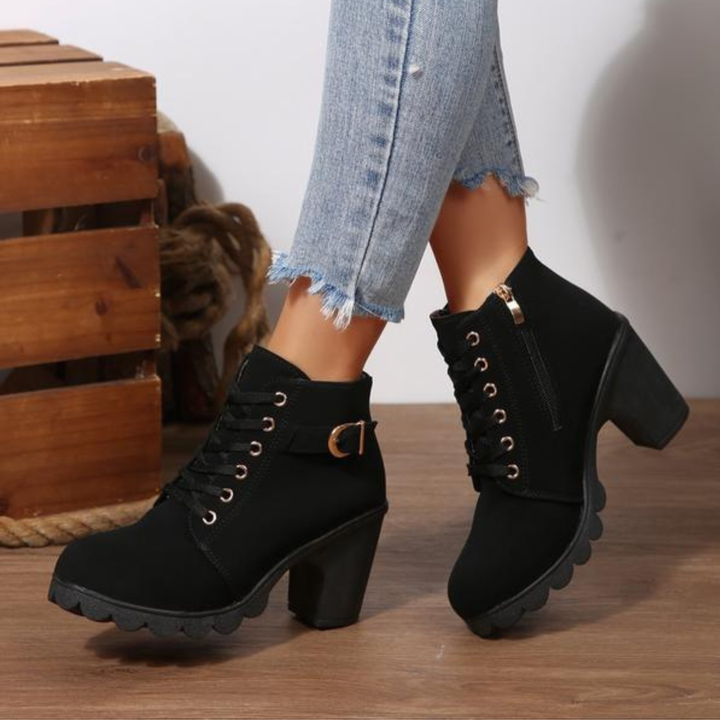 Side profile view of a woman wearing black chunky ankle boots, showcasing the lace-up and metal buckle details.
