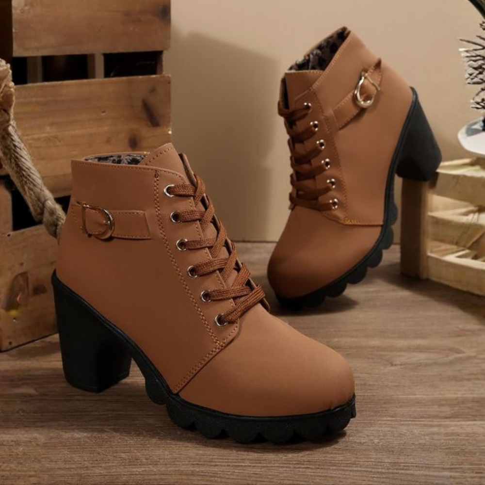 Close-up detail of the front of a black chunky ankle boot, highlighting the intricate lacing and shiny buckle.