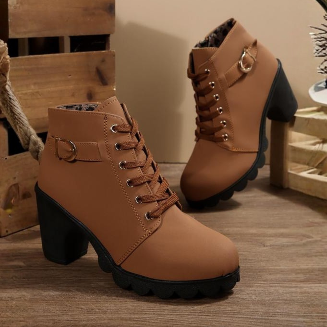 Close-up detail of the front of a black chunky ankle boot, highlighting the intricate lacing and shiny buckle.