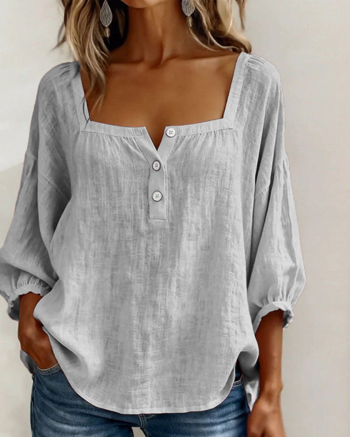 Full length view of a model wearing the gray square neck blouse, paired with white trousers.