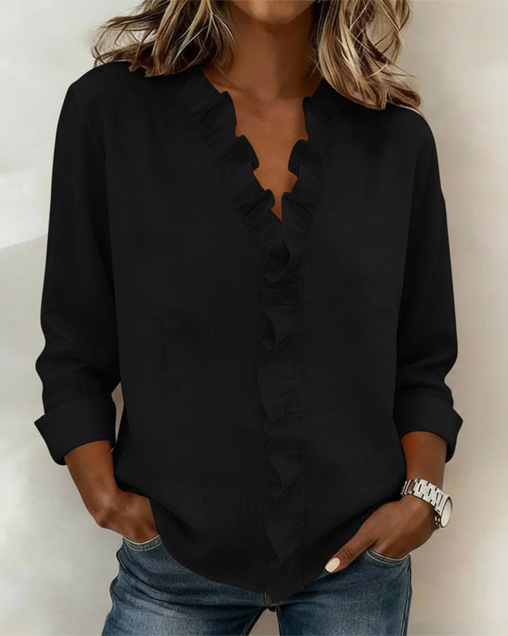 Lifestyle image of a woman casually posing in the white ruffled V-neck blouse outdoors.