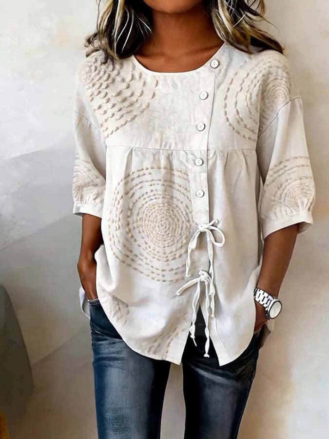 Close-up detail of the Isolde artisan embroidered top's asymmetric button placket and delicate raised stitching on the cream fabric.