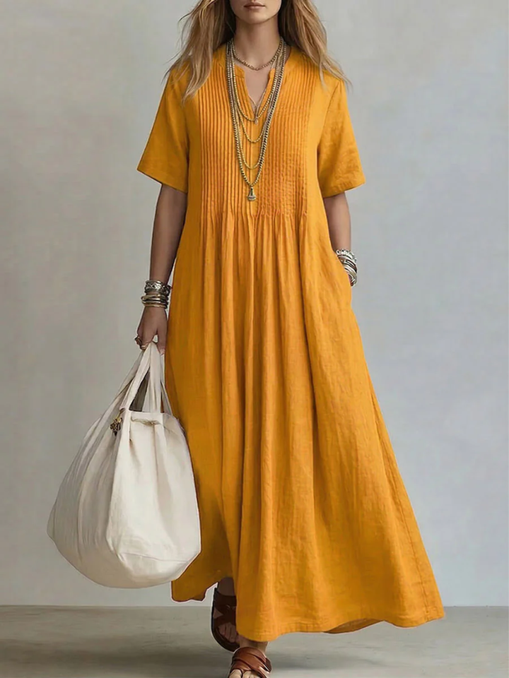 Back view of the blue pleated maxi dress, emphasizing the relaxed fit and long hemline against a natural backdrop.