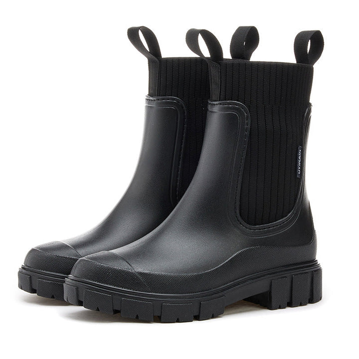 A person wearing black waterproof ankle boots while holding an umbrella, suggesting protection from rain.