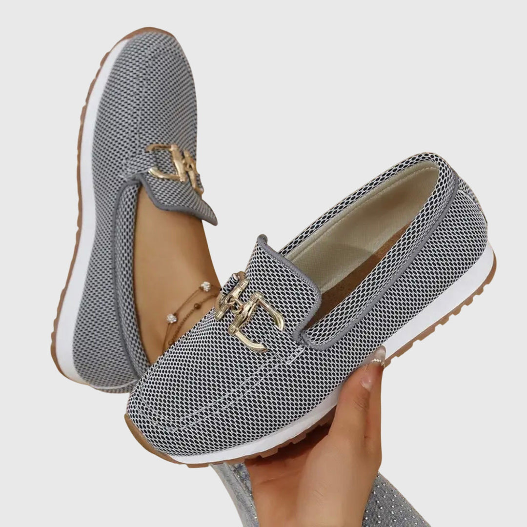Lifestyle image of a woman sitting on a bench, wearing the blue orthopedic loafer sneakers, looking relaxed and stylish.